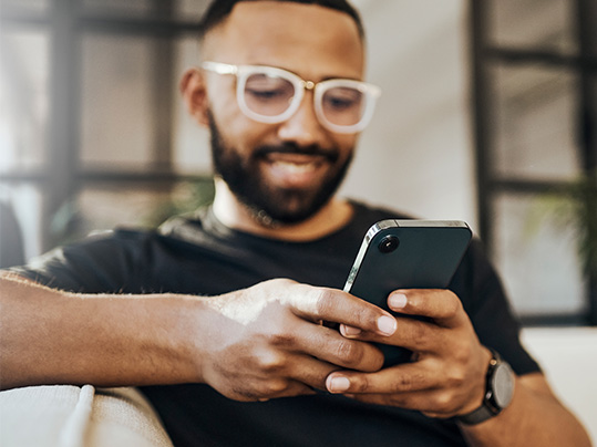Man with glasses smiling holding a smartphone