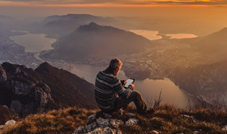Man at the top of a mountain looking at a tablet