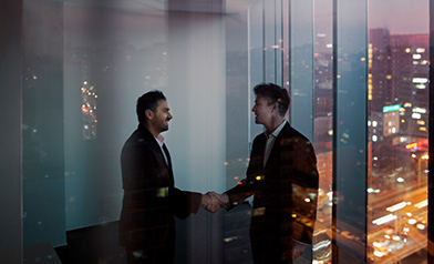 two businessmen in a window office at night shaking hands